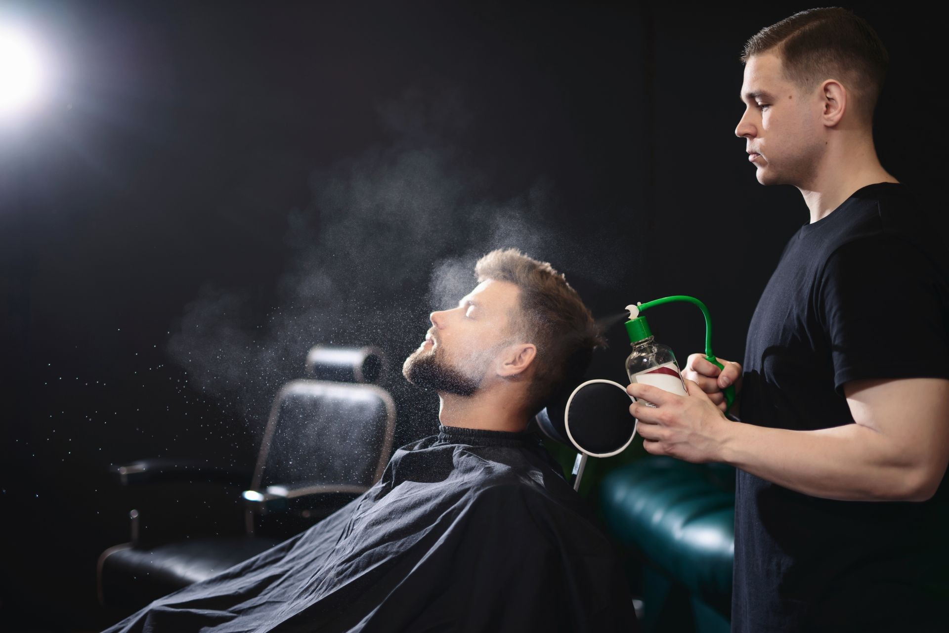 Barber sprinkles hair on the spray gun and combs his hair to a young guy with a beard and mustache. Barber Shop. Barber sprinkles hair on the spray gun and combs his hair to a young guy with a beard and mustache. Barber Shop.